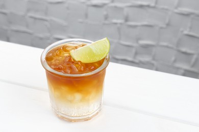 Photo of Refreshing espresso tonic drink with slice of lime on white wooden table, space for text