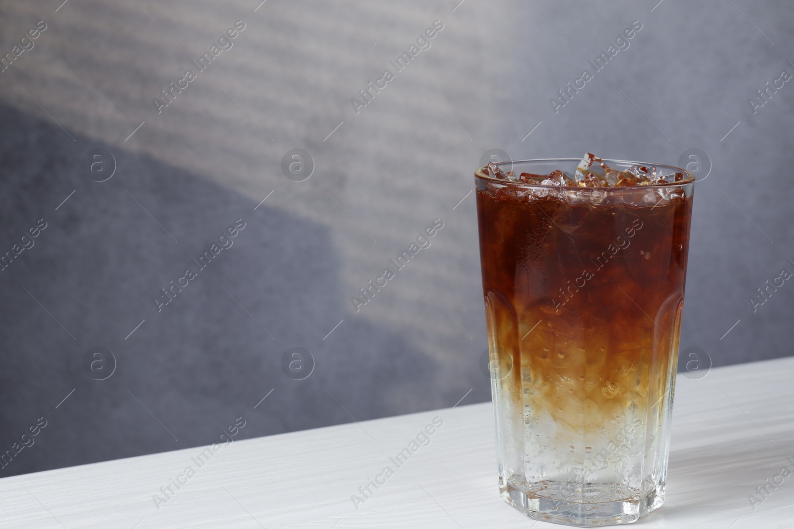 Photo of Refreshing espresso tonic drink on white wooden table, space for text