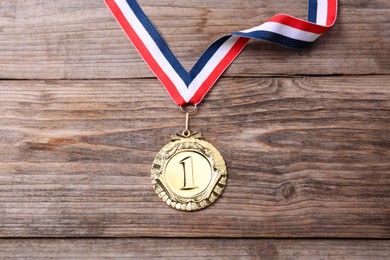 Photo of Golden medal with striped ribbon on wooden background, top view