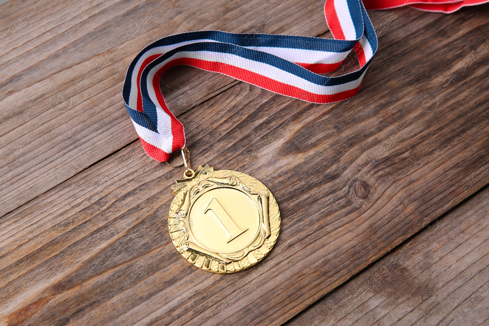 Photo of Golden medal with striped ribbon on wooden background, closeup