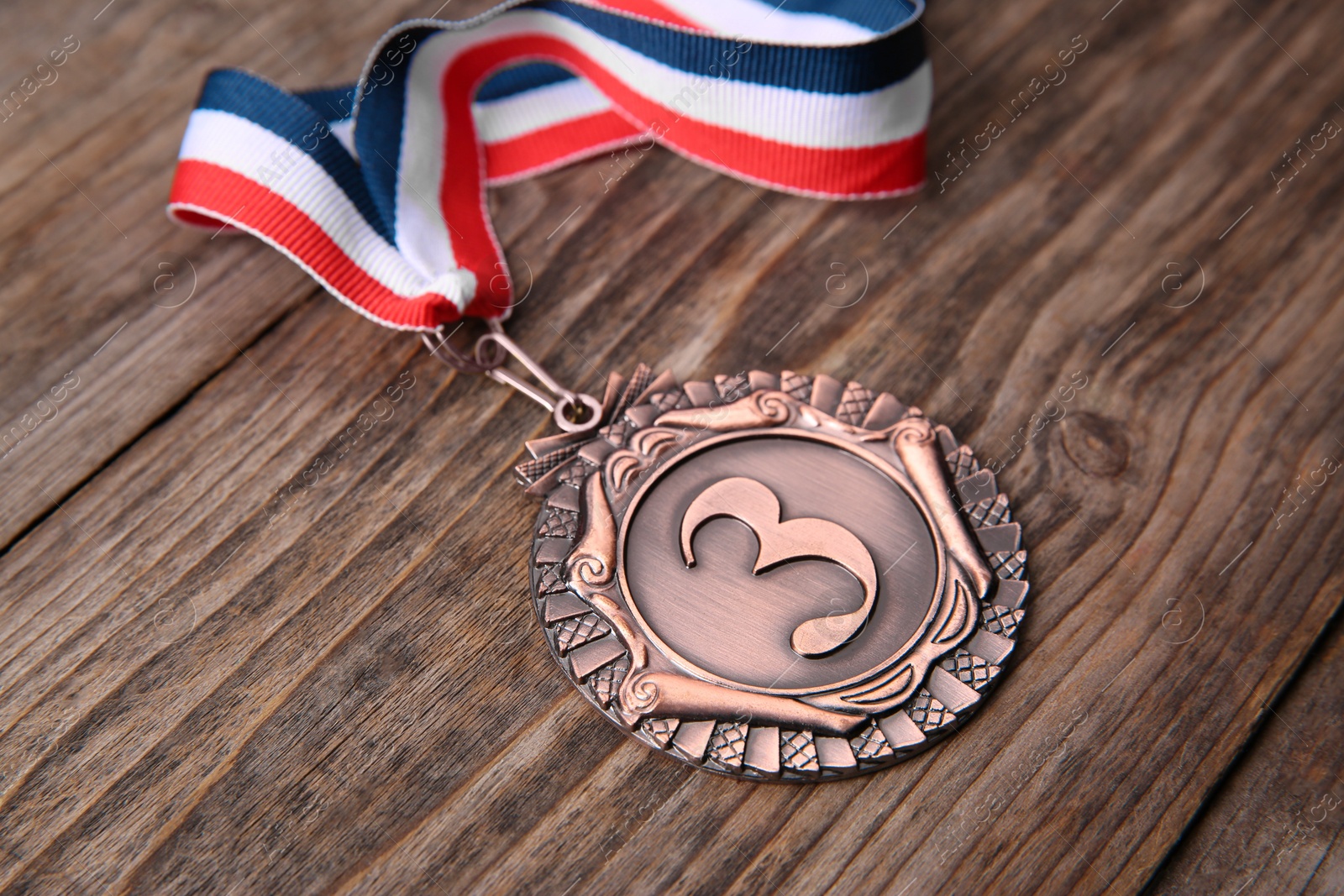 Photo of Bronze medal with striped ribbon on wooden background, closeup