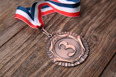 Photo of Bronze medal with striped ribbon on wooden background, closeup