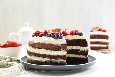 Photo of Delicious chocolate sponge cake with berries served on white wooden table, closeup