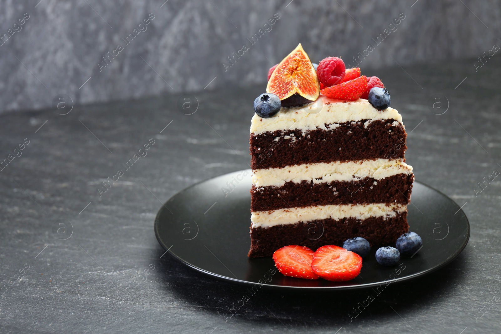 Photo of Piece of delicious chocolate sponge cake with berries on black table, closeup