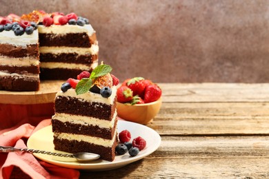 Photo of Piece of delicious chocolate sponge cake with berries served on wooden table, space for text