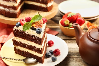 Photo of Piece of delicious chocolate sponge cake with berries served on wooden table, closeup