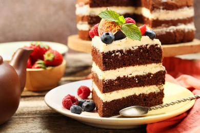 Photo of Piece of delicious chocolate sponge cake with berries served on wooden table, closeup