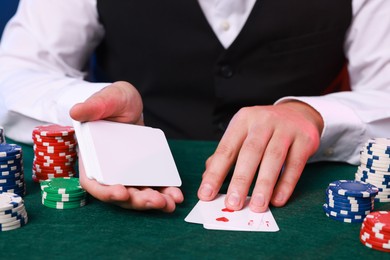 Professional croupier with playing cards at gambling table, closeup