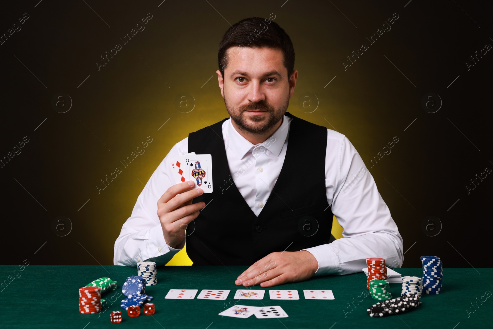 Photo of Professional croupier with playing cards at gambling table on dark yellow background