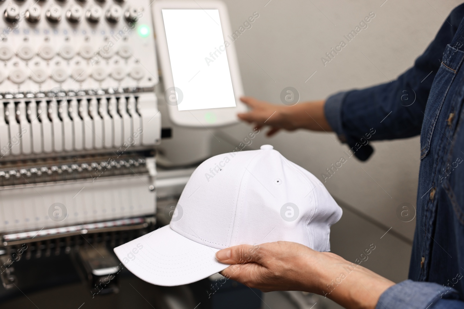 Photo of Woman with blank baseball cap for print using embroidery machine indoors, closeup