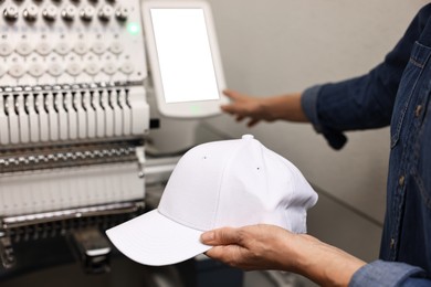 Photo of Woman with blank baseball cap for print using embroidery machine indoors, closeup