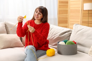 Beautiful woman knitting on sofa at home