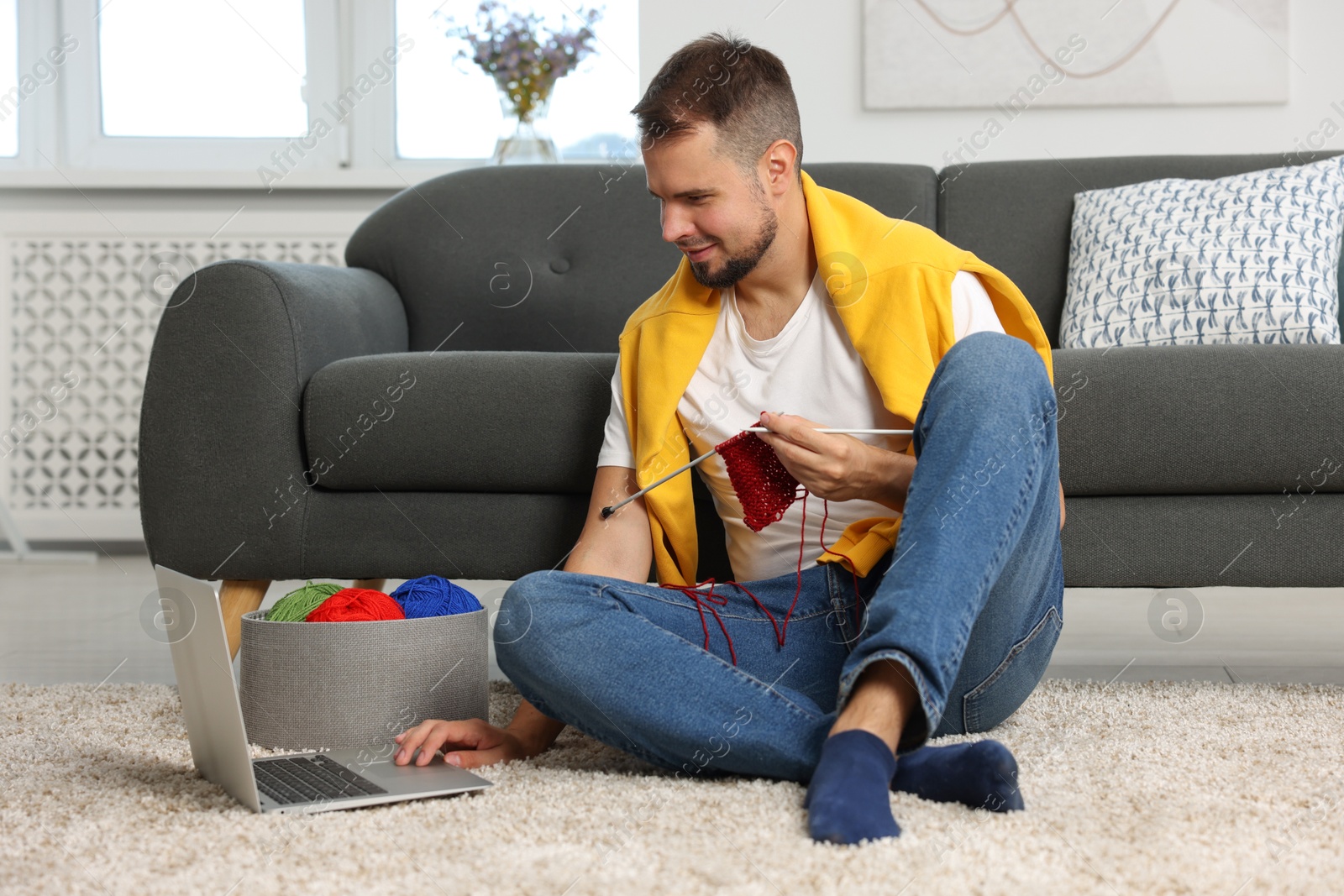 Photo of Man learning to knit with online course on floor at home