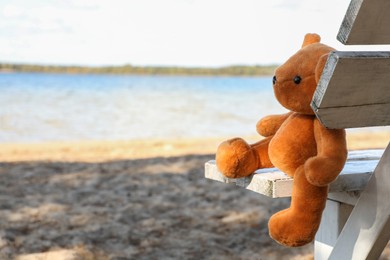 Lonely teddy bear on bench near river, space for text