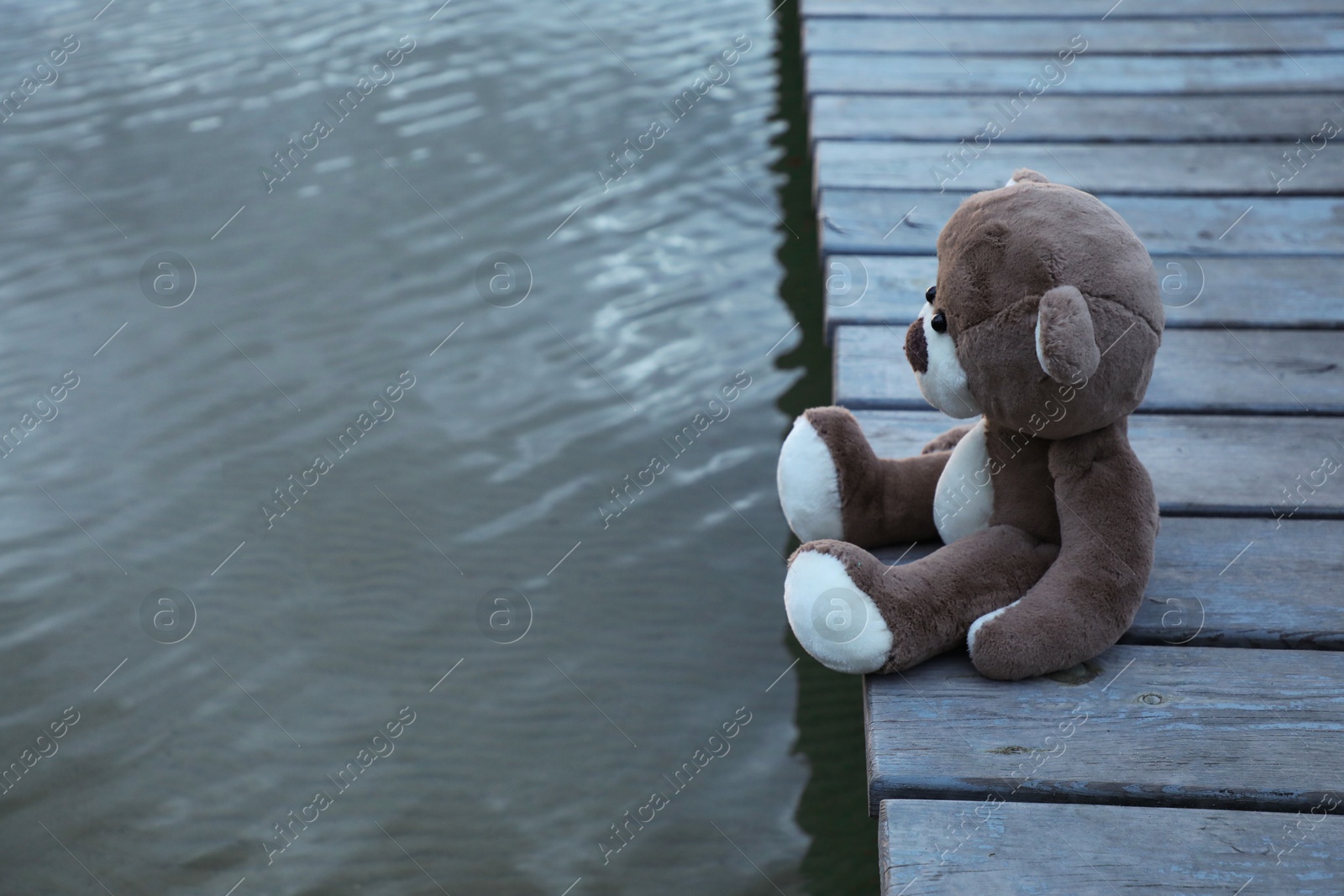 Photo of Lonely teddy bear on deck near river, space for text