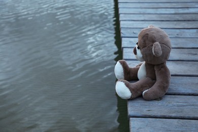 Photo of Lonely teddy bear on deck near river, space for text