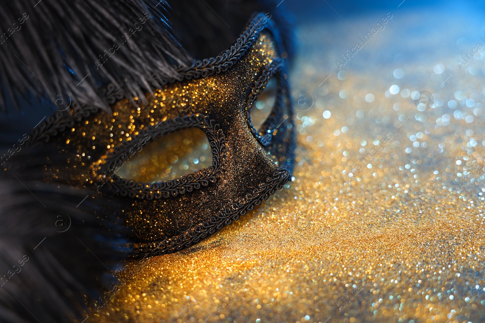 Photo of Beautiful carnival mask and black feathers on glitter background, closeup. Space for text