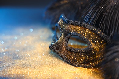 Photo of Beautiful carnival mask and black feathers on glitter background, closeup. Space for text