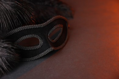 Photo of Beautiful carnival mask and feathers on black background in color lights, closeup. Space for text