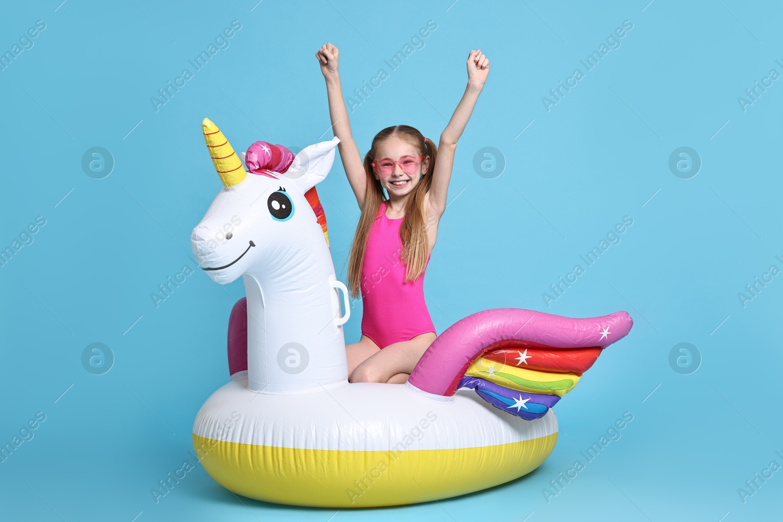 Photo of Happy little girl in beachwear with inflatable unicorn shaped ring on light blue background