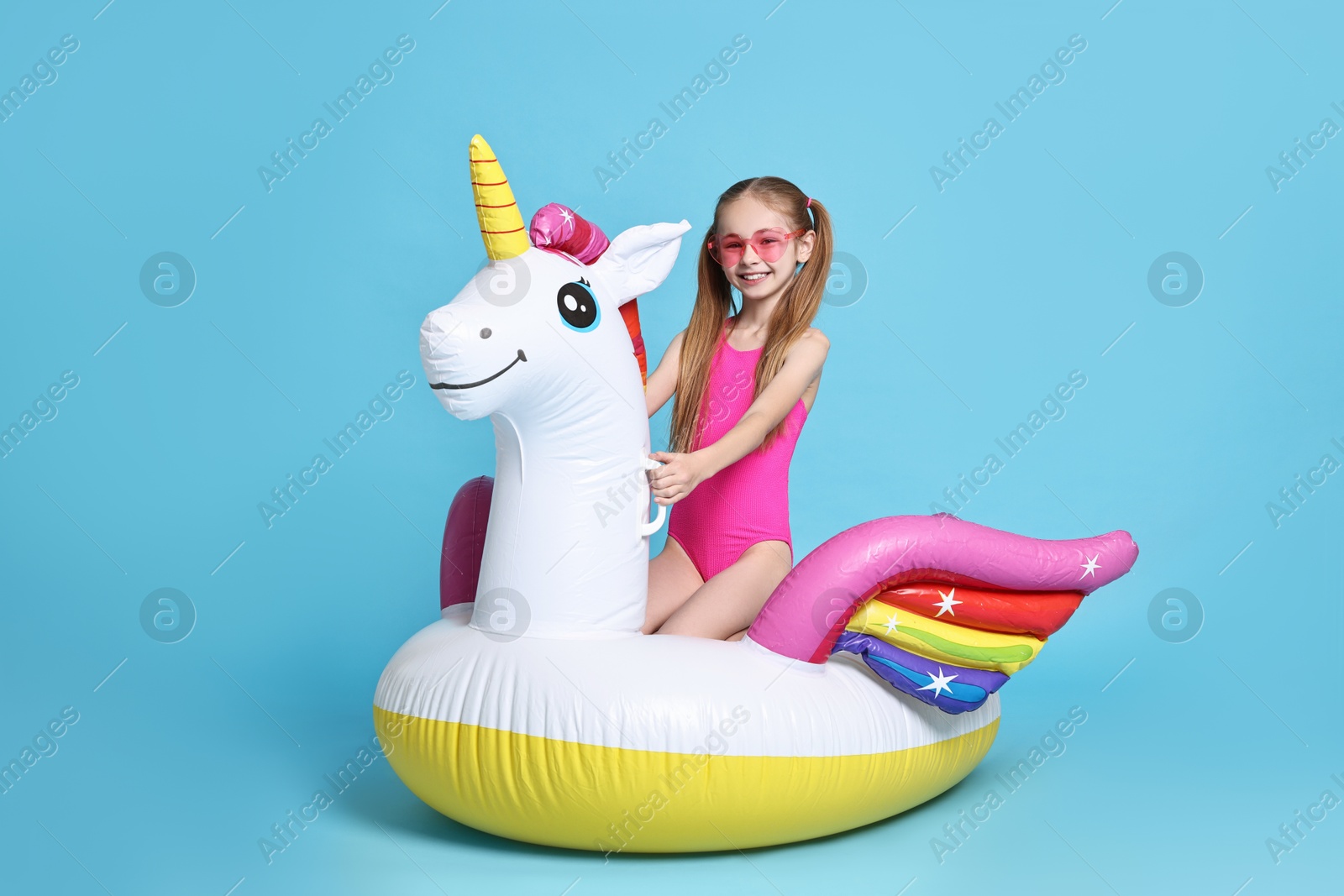 Photo of Happy little girl in beachwear with inflatable unicorn shaped ring on light blue background