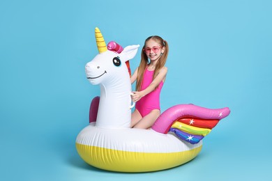 Photo of Happy little girl in beachwear with inflatable unicorn shaped ring on light blue background