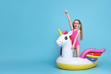 Photo of Happy little girl in beachwear with inflatable unicorn shaped ring on light blue background, space for text