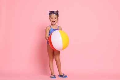 Photo of Cute little girl in swimsuit with inflatable ball on light pink background