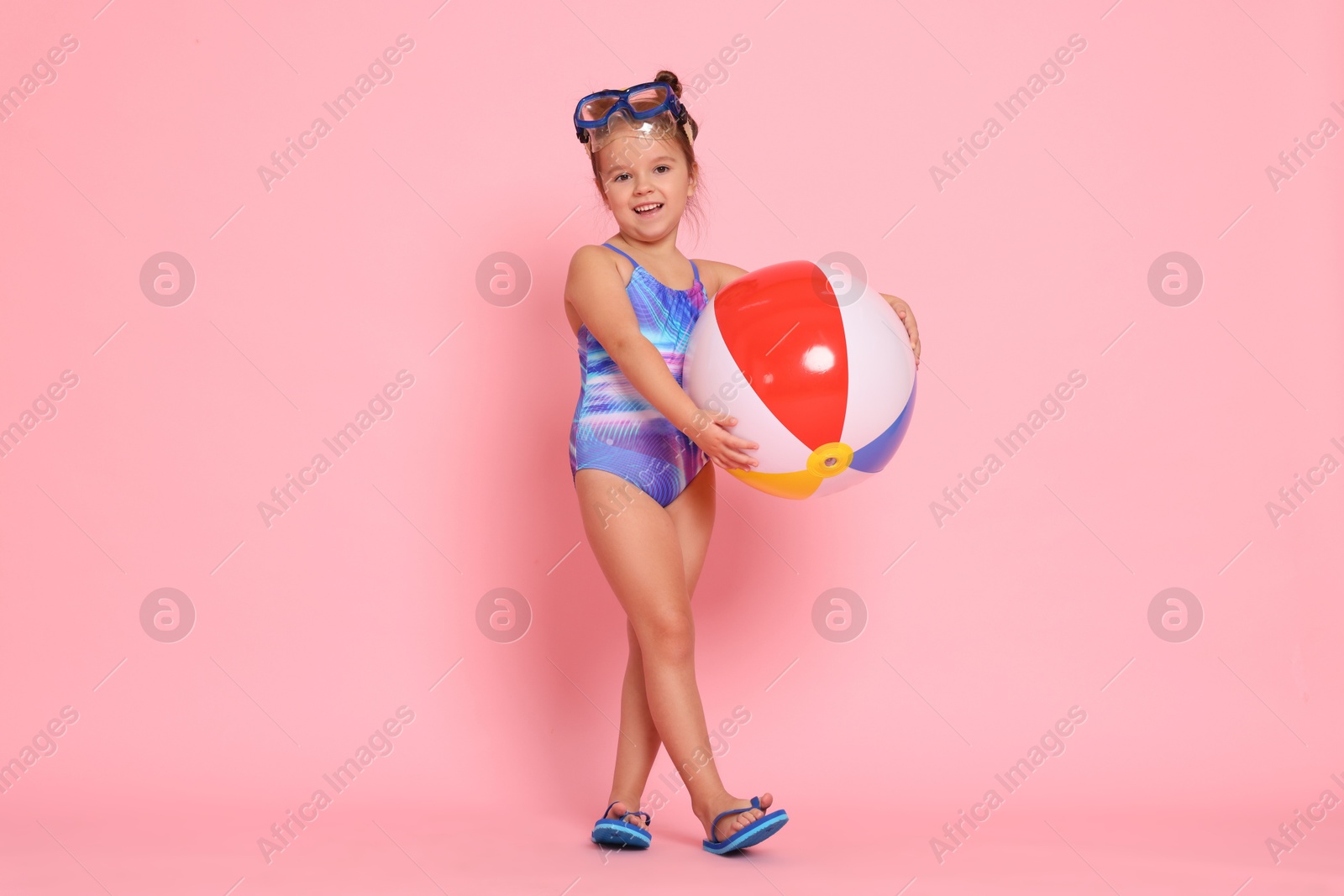 Photo of Cute little girl in swimsuit with inflatable ball on light pink background