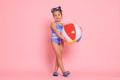 Photo of Cute little girl in swimsuit with inflatable ball on light pink background