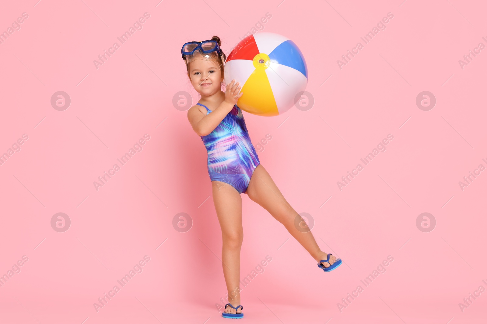 Photo of Cute little girl in swimsuit with inflatable ball on light pink background