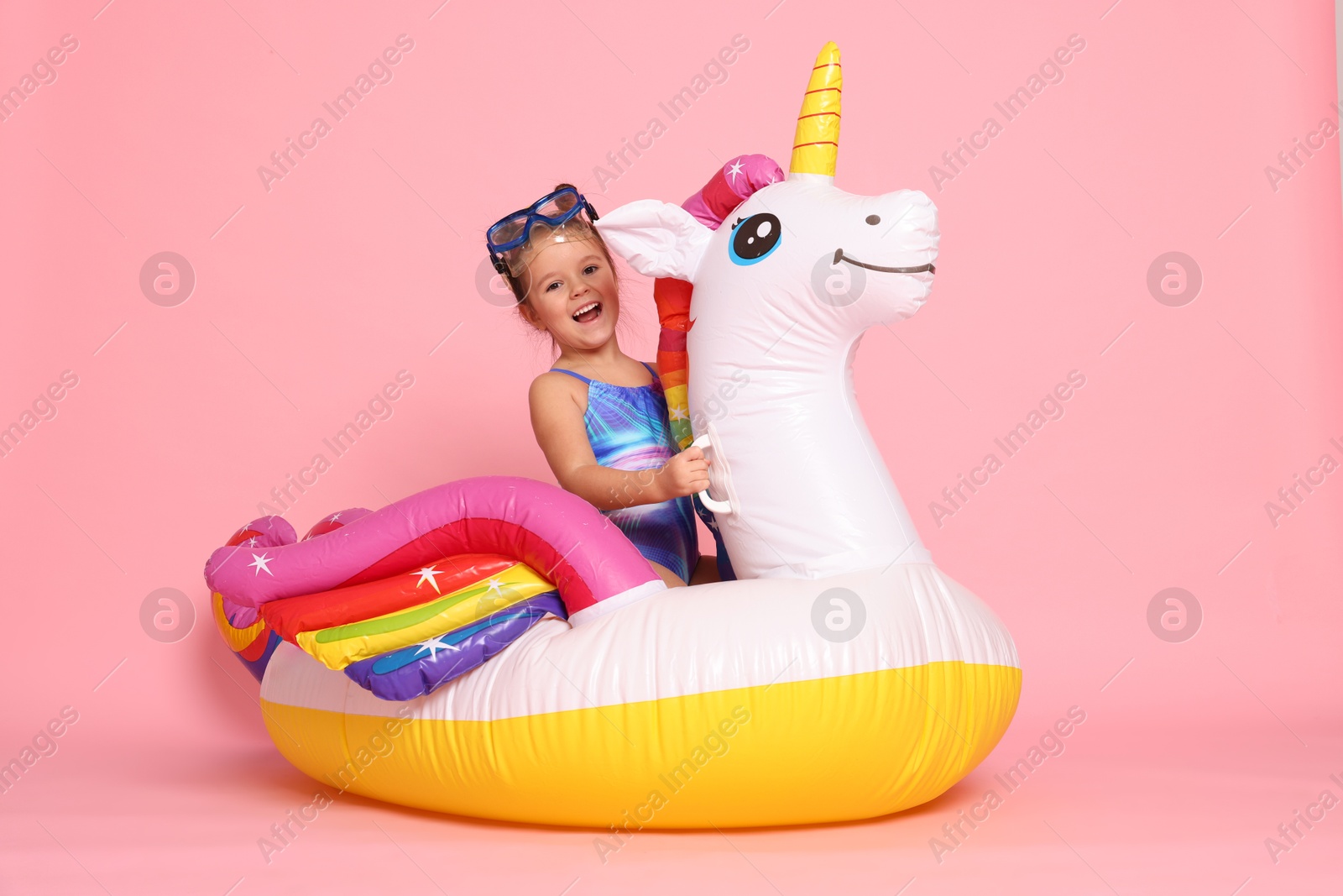 Photo of Cute little girl in swimsuit with unicorn pool float on light pink background