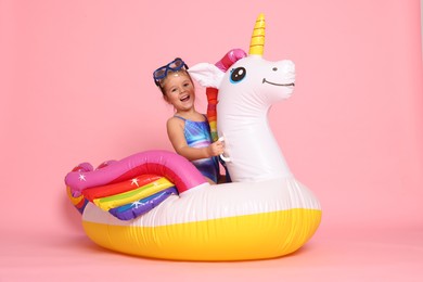 Photo of Cute little girl in swimsuit with unicorn pool float on light pink background