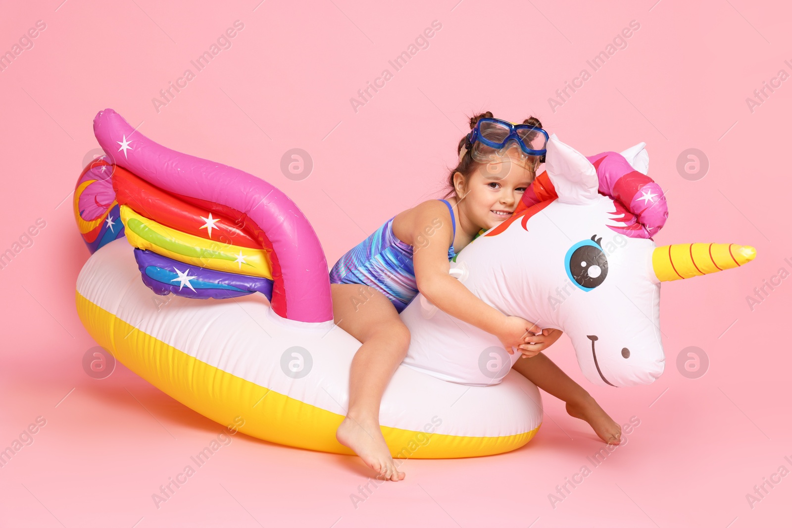 Photo of Cute little girl in swimsuit with unicorn pool float on light pink background