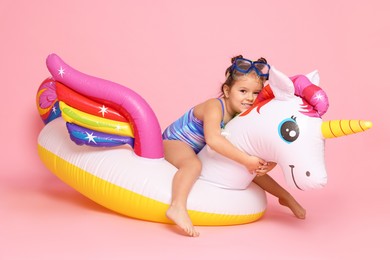 Cute little girl in swimsuit with unicorn pool float on light pink background