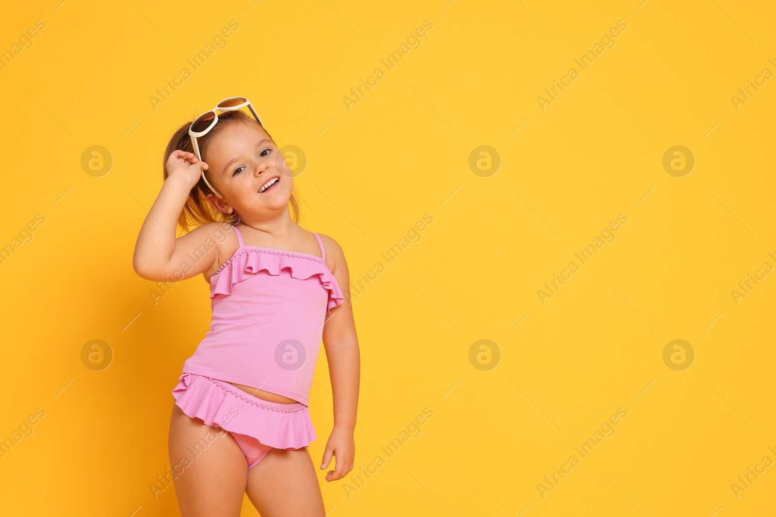 Photo of Cute little girl in swimsuit on orange background. Space for text