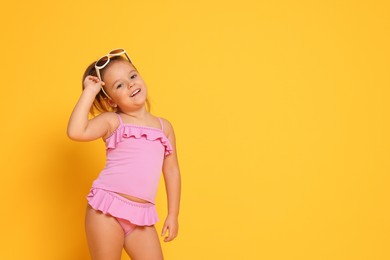 Cute little girl in swimsuit on orange background. Space for text