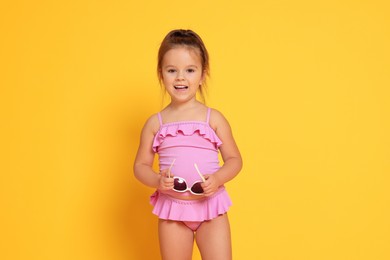 Cute little girl in swimsuit on orange background