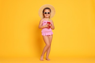 Photo of Cute little girl in swimsuit and straw hat with drink on orange background