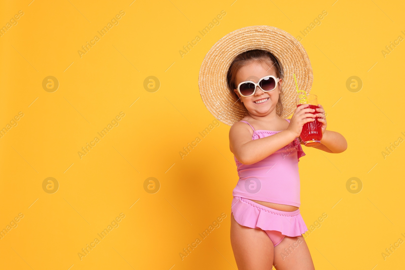 Photo of Cute little girl in swimsuit and straw hat with drink on orange background. Space for text