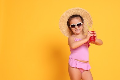 Photo of Cute little girl in swimsuit and straw hat with drink on orange background. Space for text