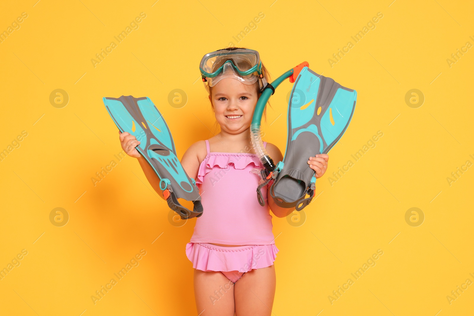 Photo of Cute little girl in swimsuit with snorkeling equipment on orange background