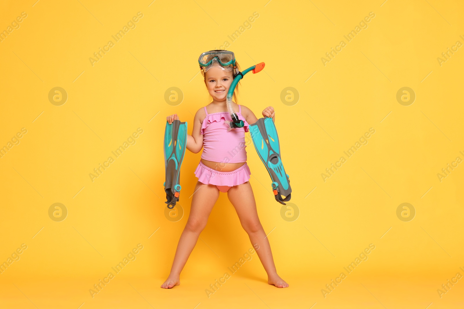 Photo of Cute little girl in swimsuit with snorkeling equipment on orange background