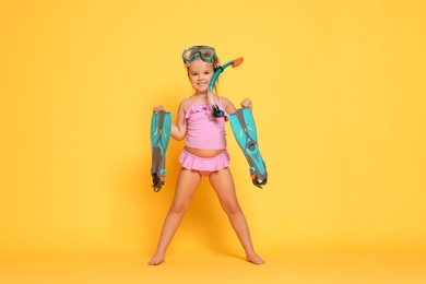 Photo of Cute little girl in swimsuit with snorkeling equipment on orange background