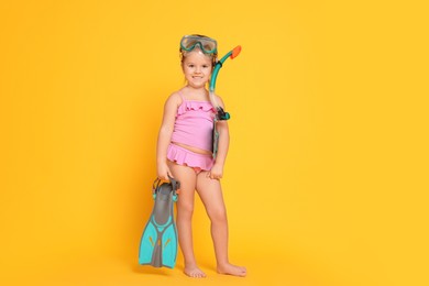 Photo of Cute little girl in swimsuit with snorkeling equipment on orange background