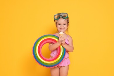 Photo of Cute little girl in swimsuit with inflatable ring eating ice cream on orange background