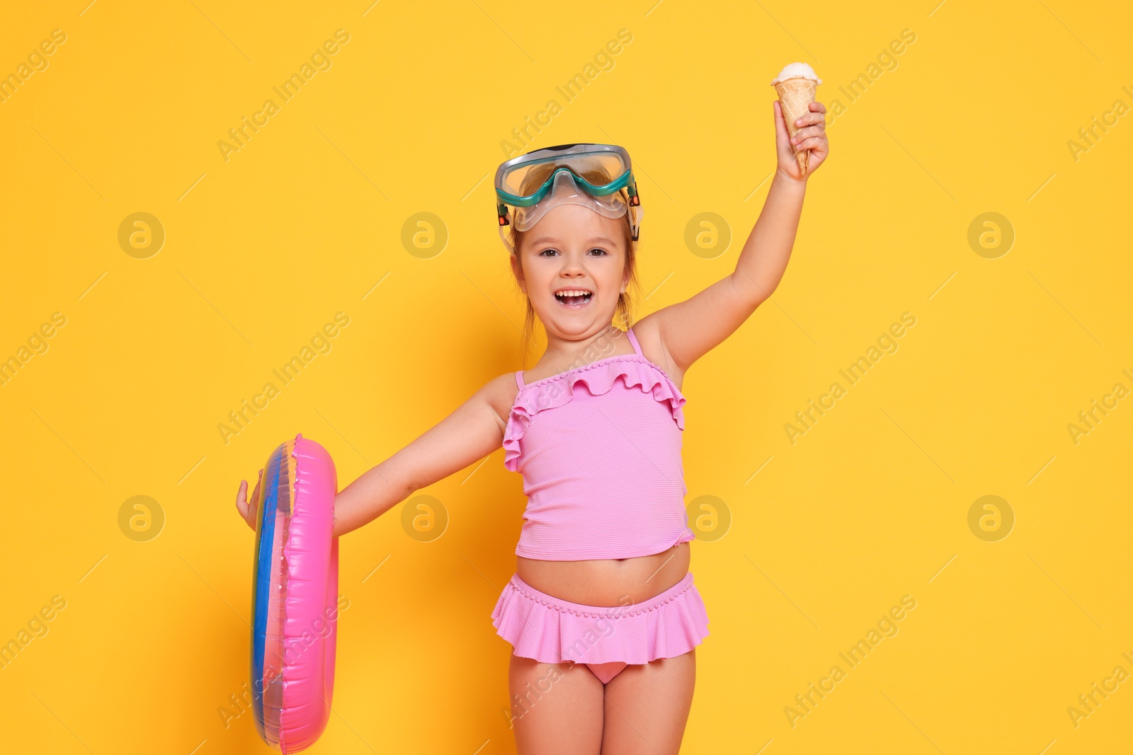 Photo of Cute little girl in swimsuit with inflatable ring eating ice cream on orange background