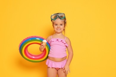 Photo of Cute little girl in swimsuit with inflatable ring eating ice cream on orange background