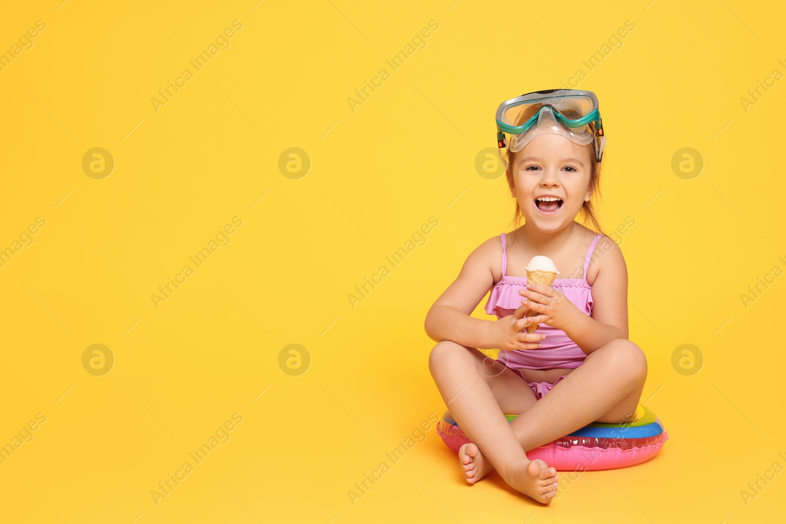 Photo of Cute little girl in swimsuit with inflatable ring eating ice cream on orange background. Space for text