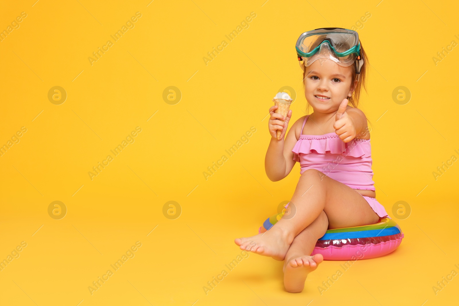 Photo of Cute little girl in swimsuit with inflatable ring eating ice cream on orange background. Space for text